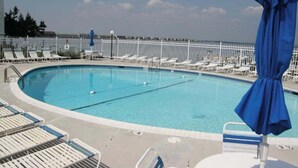 A pool area with lounge chairs and umbrellas, surrounded by a white fence. - Thunder Island 28A (Ocean City)