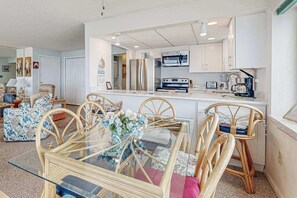 A modern kitchen with white cabinets, stainless steel appliances, and a glass dining table with wicker chairs. - Thunder Island 25A (Ocean City)
