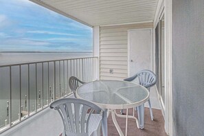 Ein Balkon mit Glastisch und Stühlen, der auf ein Gewässer blickt.