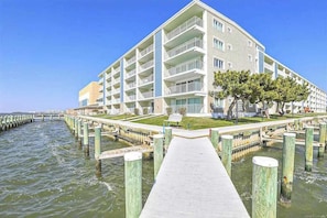 A multi-story hotel with balconies, a waterfront view, and a wooden dock extending into the water. - Thunder Island 25A (Ocean City)