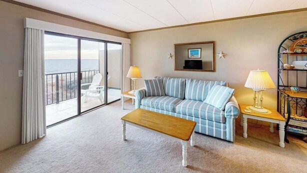 Een woonkamer met een bank, een houten salontafel, twee lampen, een televisie en een balkon met uitzicht.