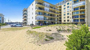 Een hotel met meerdere verdiepingen en balkons, een zandstrand ervoor, en een helderblauwe lucht.