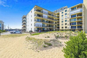 Ein mehrstöckiges Hotel mit Balkonen, einem Sandstrand davor und einem strahlend blauen Himmel.