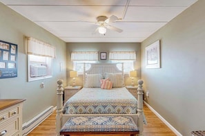 A bedroom with a bed, bedside tables, a ceiling fan, and a window with curtains. - Bay Colony 36 (Ocean City)