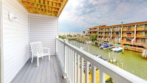A balcony with a white chair, a wooden ceiling, and a view of a marina with boats and buildings. - Dawn's Cove F (Ocean City)