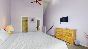 Een slaapkamer met een bed, een houten dressoir, een televisie en een plafondventilator.