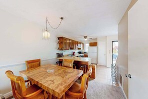 Un comedor con una mesa y sillas de madera, una cocina al fondo y un ventilador de techo.