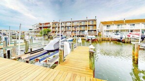 A marina with docked boats, a wooden pier, and multi-story buildings in the background. - Dawn's Cove F (Ocean City)