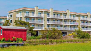 A multi-story residential building with balconies, a red shed, and a water body in the foreground. - Lucayan 18 (Ocean City)