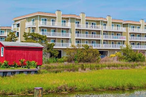 A multi-story residential building with balconies, a red shed, and a water body in the foreground. - Lucayan 18 (Ocean City)