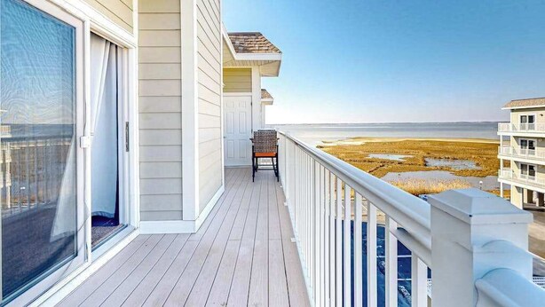 A balcony with a view of the beach, a chair, and a building with a white facade. - Lucayan 18 (Ocean City)