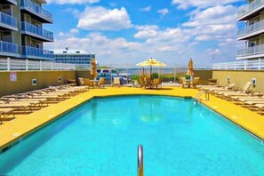 A swimming pool with sun loungers and umbrellas, surrounded by a fence and buildings. - Lucayan 18 (Ocean City)