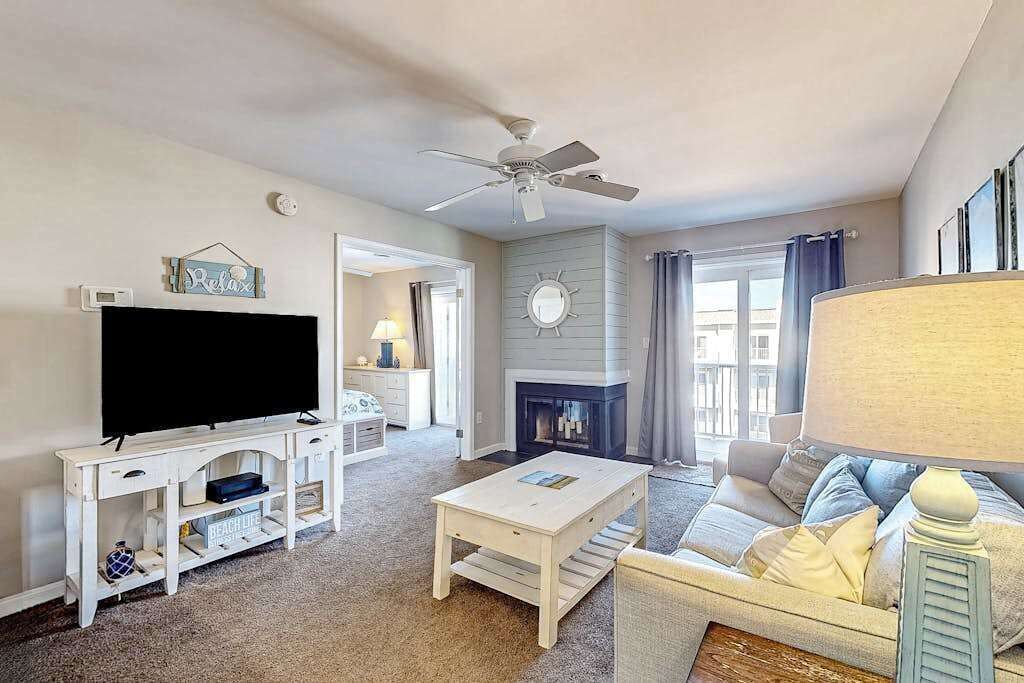 A living room with a television, white furniture, a fireplace, and a ceiling fan.
