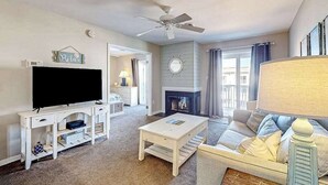 A living room with a television, white furniture, a fireplace, and a ceiling fan. - Lucayan 18 (Ocean City)