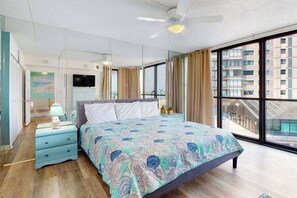A bedroom with a bed, a nightstand, a TV, and large windows. - Condo in Ocean City with pools, gym, & game room (Ocean City)