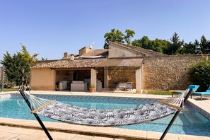 Ein Pool mit einer Hängematte, einer Steinsäule und einer überdachten Veranda.