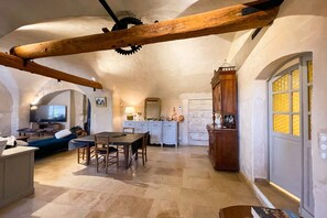 Ein rustikales Interieur mit Essbereich, Küche und Wohnbereich, gekennzeichnet durch freiliegende Holzbalken und Steinwände.