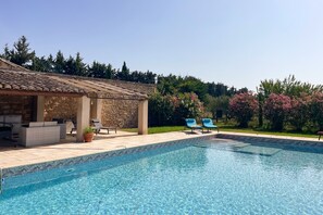 Ein Pool mit Liegestühlen, einer überdachten Sitzgelegenheit und einer Steinmauer.