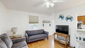 A living room with a sofa, a television, a wooden coffee table, and a ceiling fan. - Comfortable condo near the beach & downtown with private balcony (Ocean City)