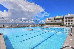 A swimming pool with clear blue water, surrounded by a building with a balcony and a view of the sea. - Stylish, single-level condo with pools, a picnic area, & private beach access (Ocean City)