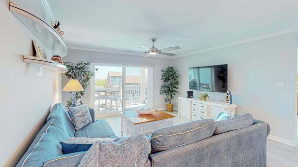 Ein modernes Wohnzimmer mit grauem Sofa, Couchtisch, Fernseher und Deckenventilator.