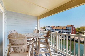 A covered balcony with a table and chairs, overlooking a marina with boats and buildings. - Baywatch III 304D (Ocean City)