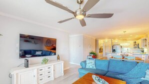Ein Wohnzimmer mit Deckenventilator, einem blauen Sofa, einem Holztisch und einem Fernseher an der Wand.