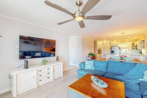 A living room with a ceiling fan, a blue sofa, a wooden coffee table, and a TV on the wall. - Baywatch III 304D (Ocean City)