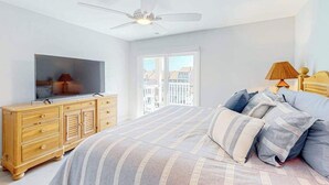 Ein Schlafzimmer mit einem Bett, einem Fernseher auf einer Holzkommode, einem Deckenventilator und einem Fenster mit Blick.