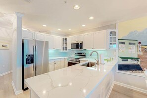 A modern kitchen with white cabinets, stainless steel appliances, a marble countertop, and a view of the ocean. - Baywatch III 304D (Ocean City)