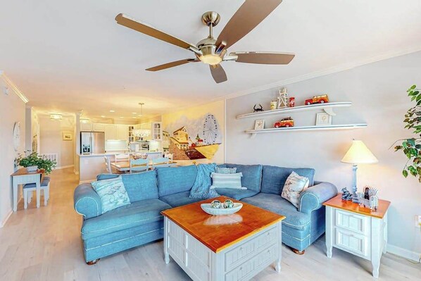 A living room with a ceiling fan, a blue sofa, a wooden coffee table, and a side table with a lamp. - Baywatch III 304D (Ocean City)