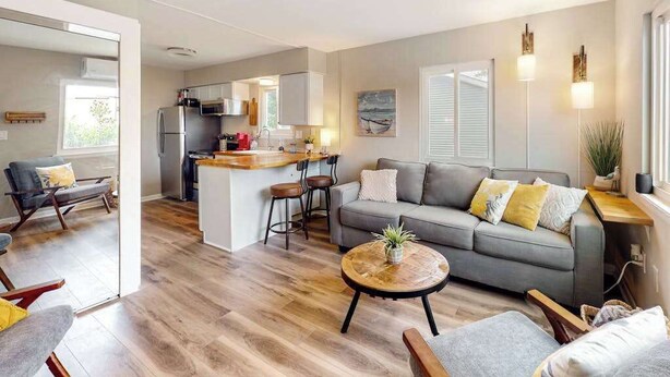 Una sala de estar moderna con un sofá gris, una mesa de centro de madera y una cocina con refrigerador y isla.