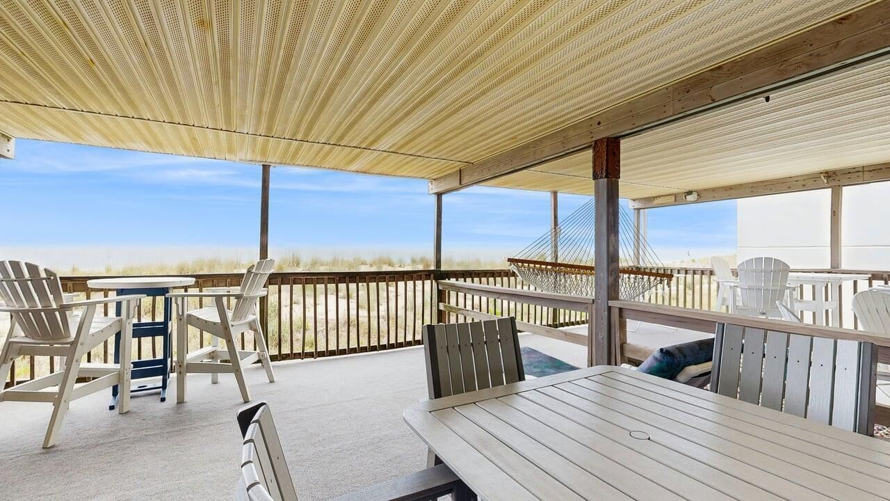 Een terras buiten met houten meubels, een zwembad en uitzicht op het strand.