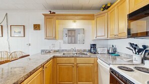 A kitchen with wooden cabinets, a granite countertop, a stove, and a sink. - Oceanfront escape close to boardwalk with balcony, W/D, and direct beach access (Ocean City)