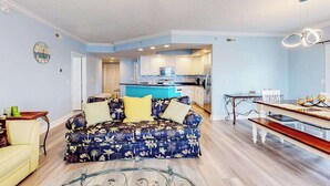 Uma sala de estar com sofá, uma mesa de jantar e uma cozinha ao fundo.