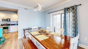 Uma sala de jantar com uma mesa de madeira, cadeiras brancas e uma luminária pendente moderna.