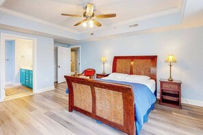 A bedroom with a wooden bed, two bedside lamps, a ceiling fan, and a door leading to another room. - 4100 #205 (Ocean City)
