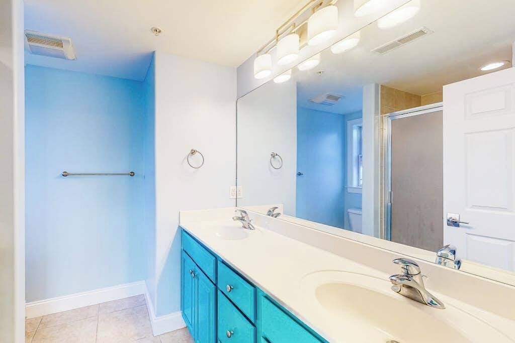Une salle de bain avec un lavabo blanc, deux robinets, un grand miroir et un porte-serviettes.