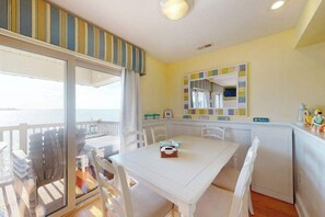 Une pièce comprenant une table à manger, des chaises, un coin cuisine et donnant sur l’extérieur grâce à une porte vitrée.