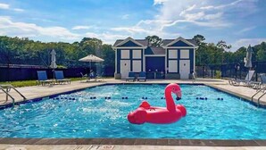 En swimmingpool med en lyserød flamingo-svømmebøje, liggestole og en bygning i baggrunden.