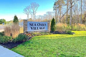 Señal de Sea Oaks Village, con base de piedra y zona ajardinada al frente.