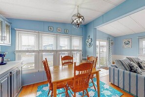 A dining area with a wooden table and chairs, a chandelier, and a view through large windows. - Assateague Pointe - 12401 Windlass Way (Berlin)