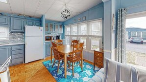 Une cuisine avec des meubles de rangement bleus, une table à manger en bois et des chaises, un réfrigérateur et une fenêtre avec des stores.