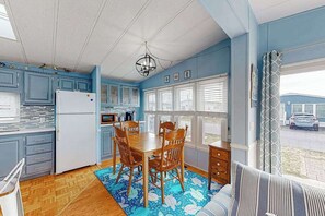 A kitchen with blue cabinets, a wooden dining table, and chairs, a refrigerator, and a window with blinds. - Assateague Pointe - 12401 Windlass Way (Berlin)