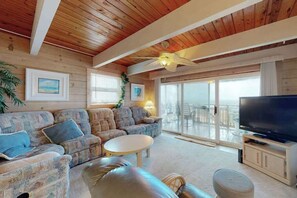 Ein Zimmer mit Holzwänden, einer Couch, einem Fernseher und einem Balkon mit Glastüren.