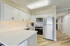 A modern kitchen with white cabinets, stainless steel appliances, and a light wood floor. - Marigot Beach 1207 (Ocean City)