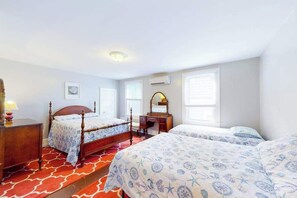 Een slaapkamer met twee bedden, een bureau, een spiegel en een raam met jaloezie ën.