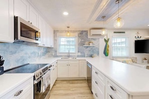 A modern kitchen with white cabinetry, a built-in oven, a microwave, and a large island with a sink. - Lands End Unit 6B (Ocean City)