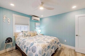 A bedroom with a bed, a chair, a ceiling fan, an air conditioning unit, and a door. - Lands End Unit 6B (Ocean City)