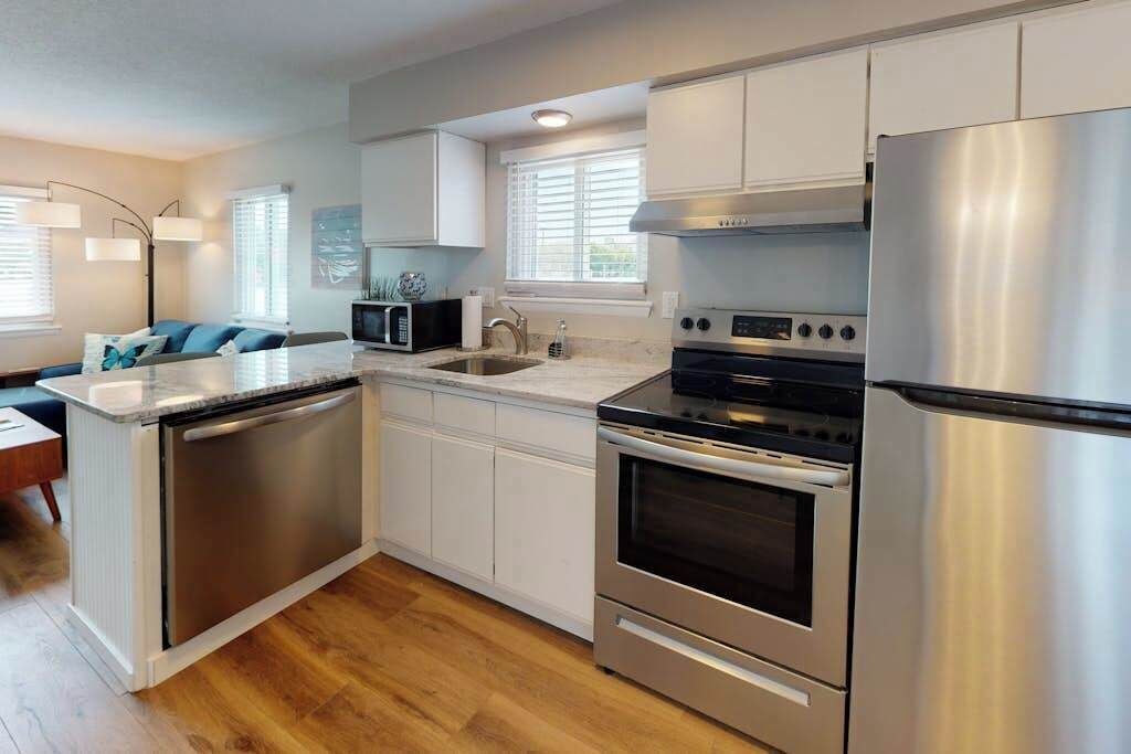 A modern kitchen with stainless steel appliances, white cabinetry, and a wooden floor.
